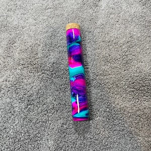 May include: A colorful glass tube with a cork top. The tube is decorated with swirls of pink, blue, and purple.