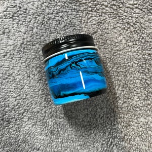 May include: A small, round, blue and black jar with a black lid. The jar has a swirling, abstract design.