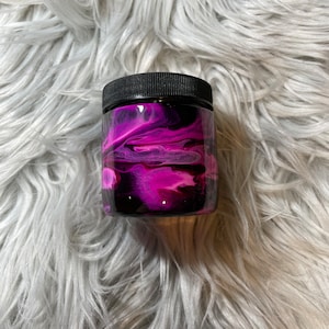 May include: A small glass jar with a black lid. The jar is decorated with pink and black swirls of paint.