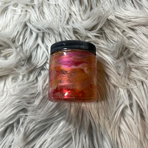 May include: A clear glass jar with a black lid filled with a glittery, multi-colored slime. The slime is a mix of pink, orange, and gold.
