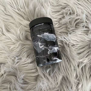 May include: Black and white marble tumbler with a black lid. The tumbler is sitting on a fluffy white surface.