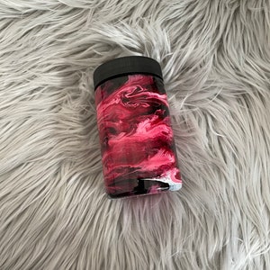 May include: A black and pink marbled tumbler with a black lid. The tumbler is on a gray fuzzy surface.