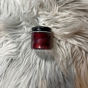 May include: A small glass jar with a black lid filled with a glittery red substance.