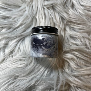 May include: A small, round jar with a black lid and a silver and black marbled design.