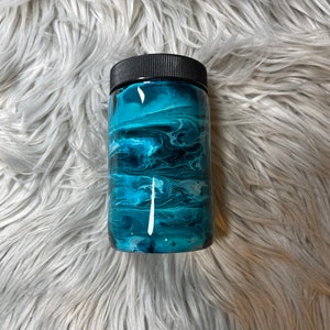 May include: A teal and black tumbler with a swirling abstract design. The tumbler has a black lid.