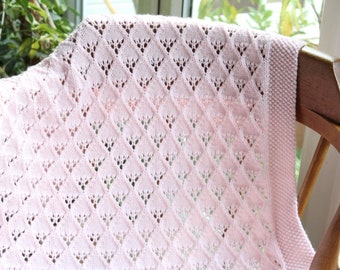 May include: A pink crocheted baby blanket with a diamond pattern. The blanket is draped over a wooden chair.