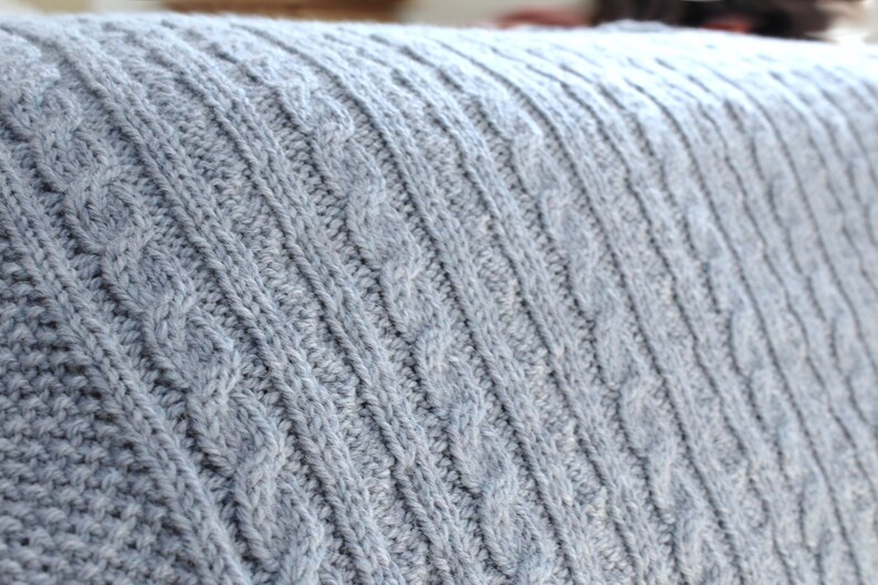 Cabled baby blanket knitting pattern. This completely reversible blanket has cables on both sides of the blanket. The moss stitch edges are knitted at the same time. Pattern written for Aran weight yarn.