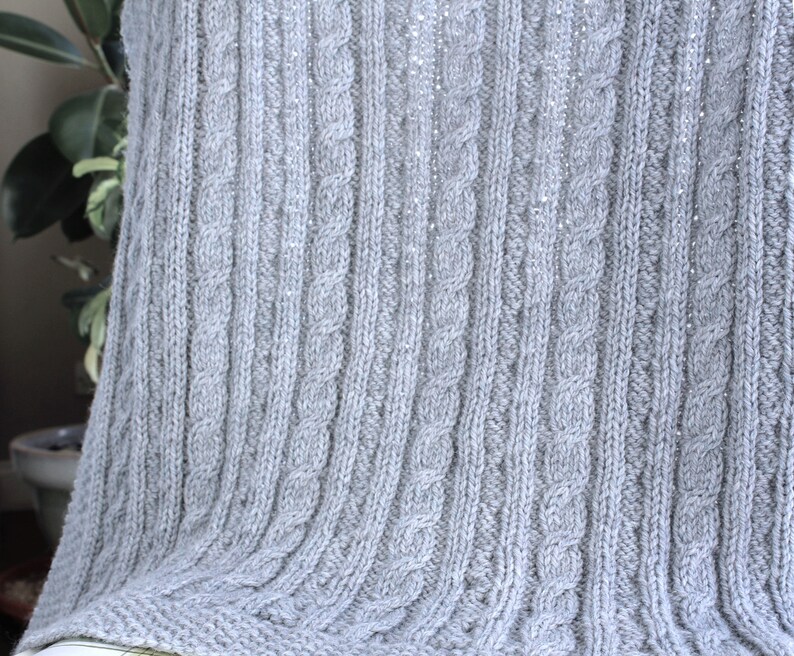 Cabled baby blanket knitting pattern. This completely reversible blanket has cables on both sides of the blanket. The moss stitch edges are knitted at the same time. Pattern written for Aran weight yarn.