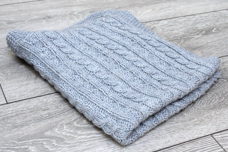 Cabled baby blanket knitting pattern. This completely reversible blanket has cables on both sides of the blanket. The moss stitch edges are knitted at the same time. Pattern written for Aran weight yarn.
