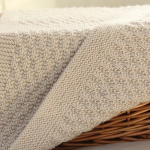 May include: A beige knitted blanket with a textured pattern, folded over a wicker basket.