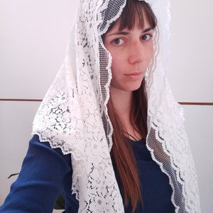 May include: A white lace veil with a floral pattern. The veil is worn over a person's head and shoulders.