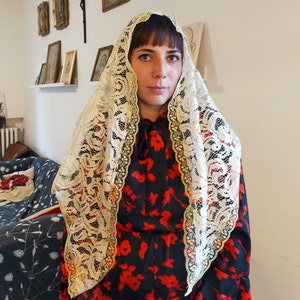 May include: A woman wearing a white lace veil over a black dress with red floral print. The veil is a traditional head covering.