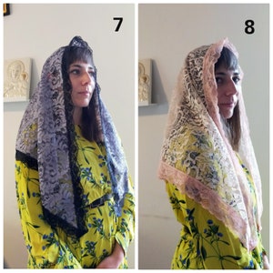May include: Two women wearing lace veils. The veil on the left is black with a gray lace pattern. The veil on the right is pink with a white lace pattern. Both women are wearing yellow floral dresses.