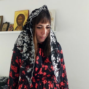 May include: A woman wearing a black and white floral dress with a black lace veil over her head. The veil has white floral embroidery.