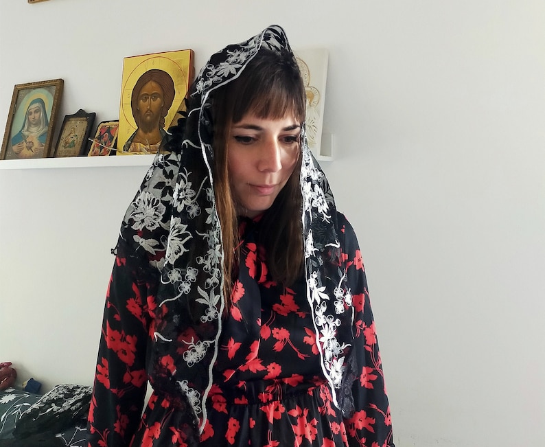 May include: A woman wearing a black and white floral dress with a black lace veil over her head. The veil has white floral embroidery.