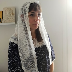 May include: White lace mantilla with a floral pattern. The mantilla is worn over a navy blue dress with white polka dots.