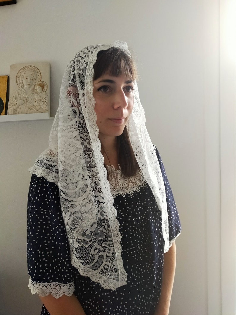 May include: White lace mantilla with a floral pattern. The mantilla is worn over a navy blue dress with white polka dots.