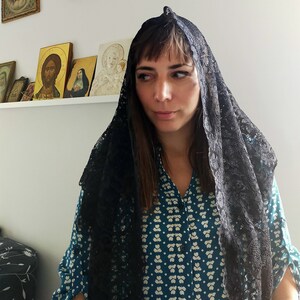 May include: A woman wearing a black lace mantilla over a teal blue patterned blouse. The woman has dark hair and is looking at the camera.