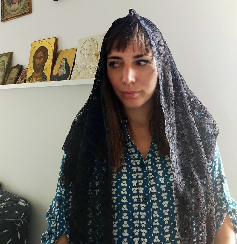 May include: A woman wearing a black lace mantilla over a teal blue patterned blouse. The woman has dark hair and is looking at the camera.
