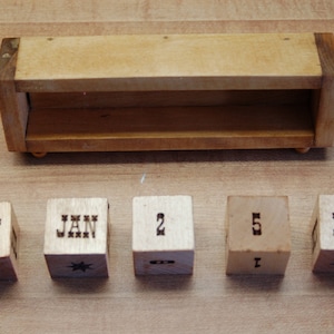 Puede incluir: Calendario perpetuo de madera clara. Incluye una estanter&iacute;a de madera y cinco bloques de madera. Los bloques muestran los meses de junio, enero y diciembre, junto con los n&uacute;meros 2 y 5. Cada bloque de mes tiene un dise&ntilde;o de estrella.