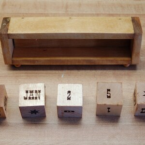 Puede incluir: Calendario perpetuo de madera con acabado marr&oacute;n claro. El calendario incluye una caja de madera y cinco cubos de madera. Los cubos muestran meses, n&uacute;meros y dise&ntilde;os de estrellas. Los meses mostrados son junio, enero y diciembre.