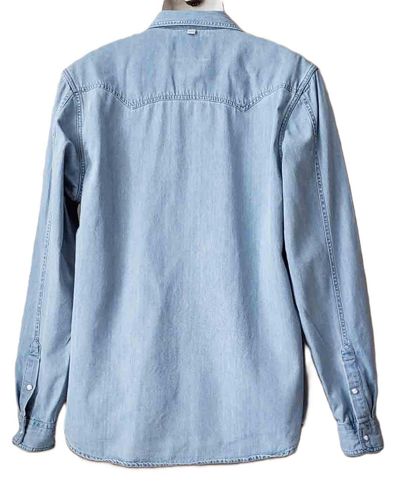 Puede incluir: Camisa vaquera azul claro de manga larga. La camisa presenta un cuello cl&aacute;sico, pu&ntilde;os abotonados y un detalle de canes&uacute; en la espalda. La mezclilla tiene un aspecto descolorido.