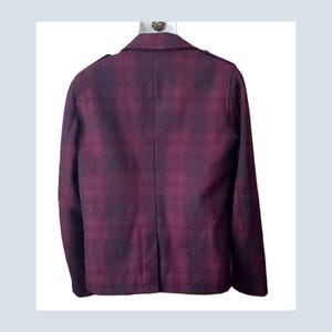 K&ouml;nnte beinhalten: Burgunderfarbener Blazer mit Karomuster, Zwei-Knopf-Verschluss und fallendem Revers. Die R&uuml;ckseite der Jacke ist sichtbar und zeigt die taillierte Passform und Schulterdetails. Der Stoff hat einen dezenten Glanz.