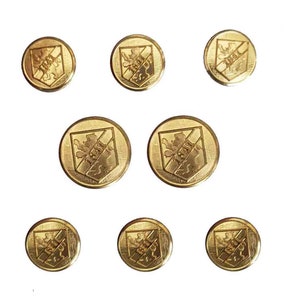 May include: A set of eight circular gold-toned metal buttons, each featuring an embossed shield design with a lion figure and the text 1841. The buttons have a polished finish and a raised border, arranged in three rows against a plain white background.