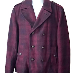 K&ouml;nnte beinhalten: Burgunderfarbene, zweireihige Jacke mit Karomuster. Die Jacke hat sechs dunkle Metallkn&ouml;pfe, zwei Vordertaschen und Schulterklappen. Die Jacke wird auf einer wei&szlig;en Schaufensterpuppe pr&auml;sentiert.