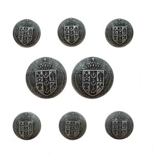 May include: A set of eight round metal buttons in a weathered silver finish. Each button features a raised crest design with a crown at the top, a shield divided into three vertical sections containing various symbols, and leafy branches on the sides.