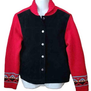 May include: A jacket featuring a black suede front panel and vibrant red knit sleeves. The garment includes a ribbed red collar, a front button closure with silver-toned buttons, and a colorful geometric pattern at the cuffs in blue, yellow, and black.