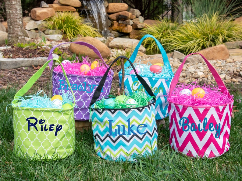May include: Four personalized Easter baskets with different colored chevron and geometric patterns. The baskets are filled with shredded paper and plastic Easter eggs. The names Riley, Luke, Bailey, and Carson are embroidered on the baskets.
