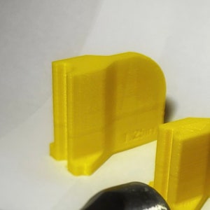 May include: A yellow plastic 3D printed object with the text "1.250" printed on the side.