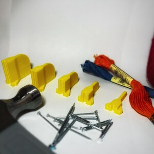 May include: A set of yellow plastic tools for crafting, including a hammer, nails, and small yellow plastic pieces. There are also two spools of embroidery floss, one red and one blue.