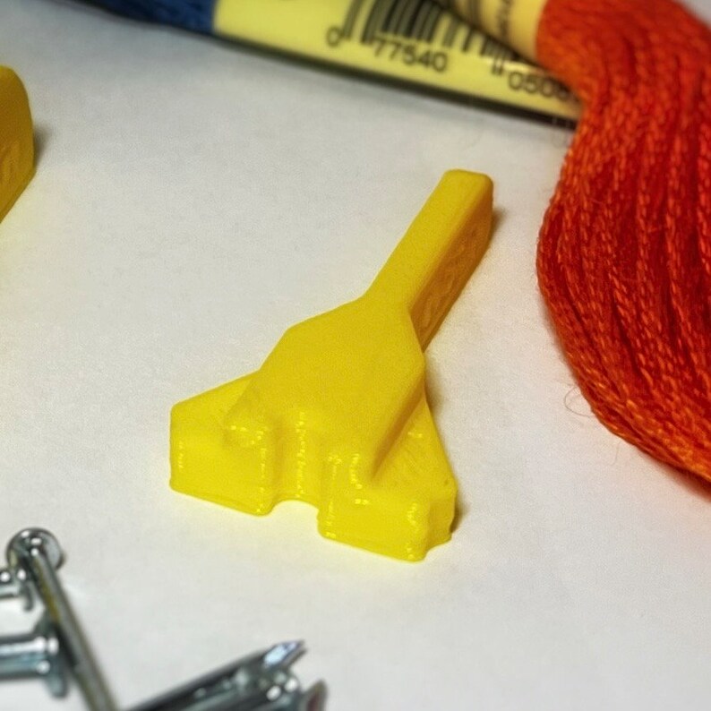 May include: A yellow plastic tool with a pointed tip and a handle. The tool is designed for use with embroidery floss.