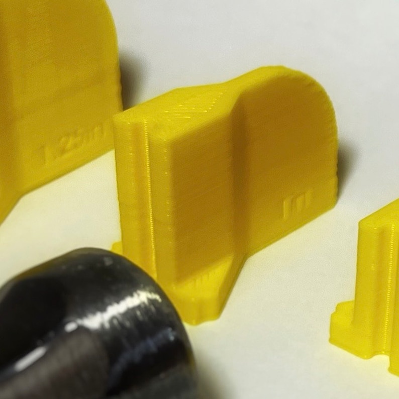 May include: Three yellow plastic 3D printed objects with rounded edges and the number "1200" printed on one of the objects.