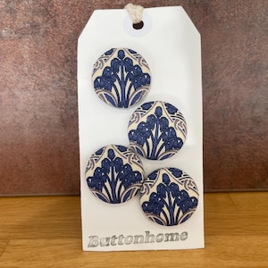 Könnte beinhalten: Vier runde Stoffknöpfe mit einem blauen und weißen Blumenmuster. Die Knöpfe werden auf einem weißen Etikett mit dem Wort "Buttonhome" darauf gezeigt.