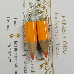 May include: A pair of orange pencil earrings with silver hooks. The earrings are made to look like real pencils with a red eraser on the end.