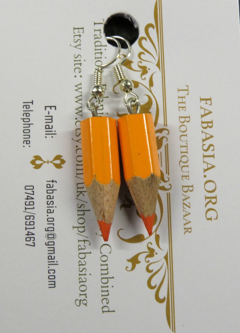 May include: A pair of orange pencil earrings with silver hooks. The earrings are made to look like real pencils with a red eraser on the end.