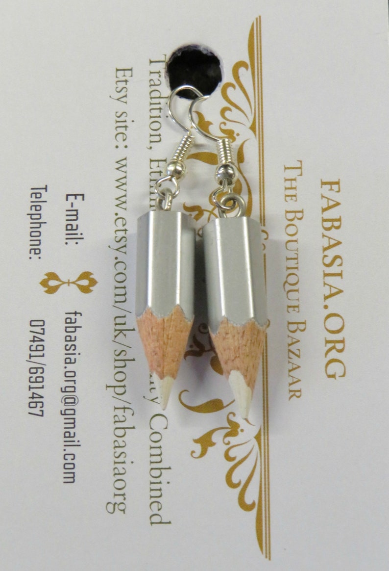 May include: A pair of silver pencil earrings with white eraser tips. The earrings are hanging from silver hooks.