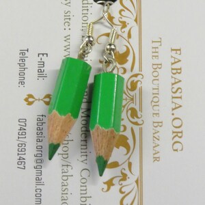 May include: A pair of green pencil earrings with silver hooks. The earrings are made to look like sharpened pencils with a wood-colored base and a green painted tip.