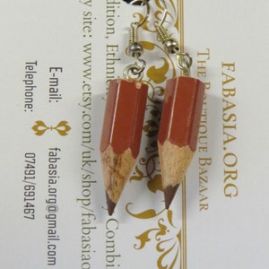 May include: A pair of earrings shaped like pencils, with brown wooden bodies and dark gray graphite tips. The earrings are hanging from silver hooks.