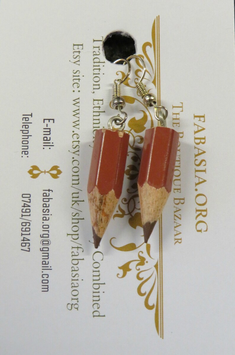 May include: A pair of earrings shaped like pencils, with brown wooden bodies and dark gray graphite tips. The earrings are hanging from silver hooks.