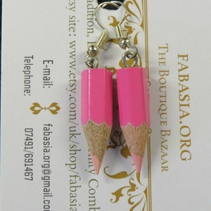 May include: A pair of pink pencil earrings with silver hooks. The pencils are made of wood and have a pink paint finish. The earrings are a fun and unique way to add a touch of personality to any outfit.