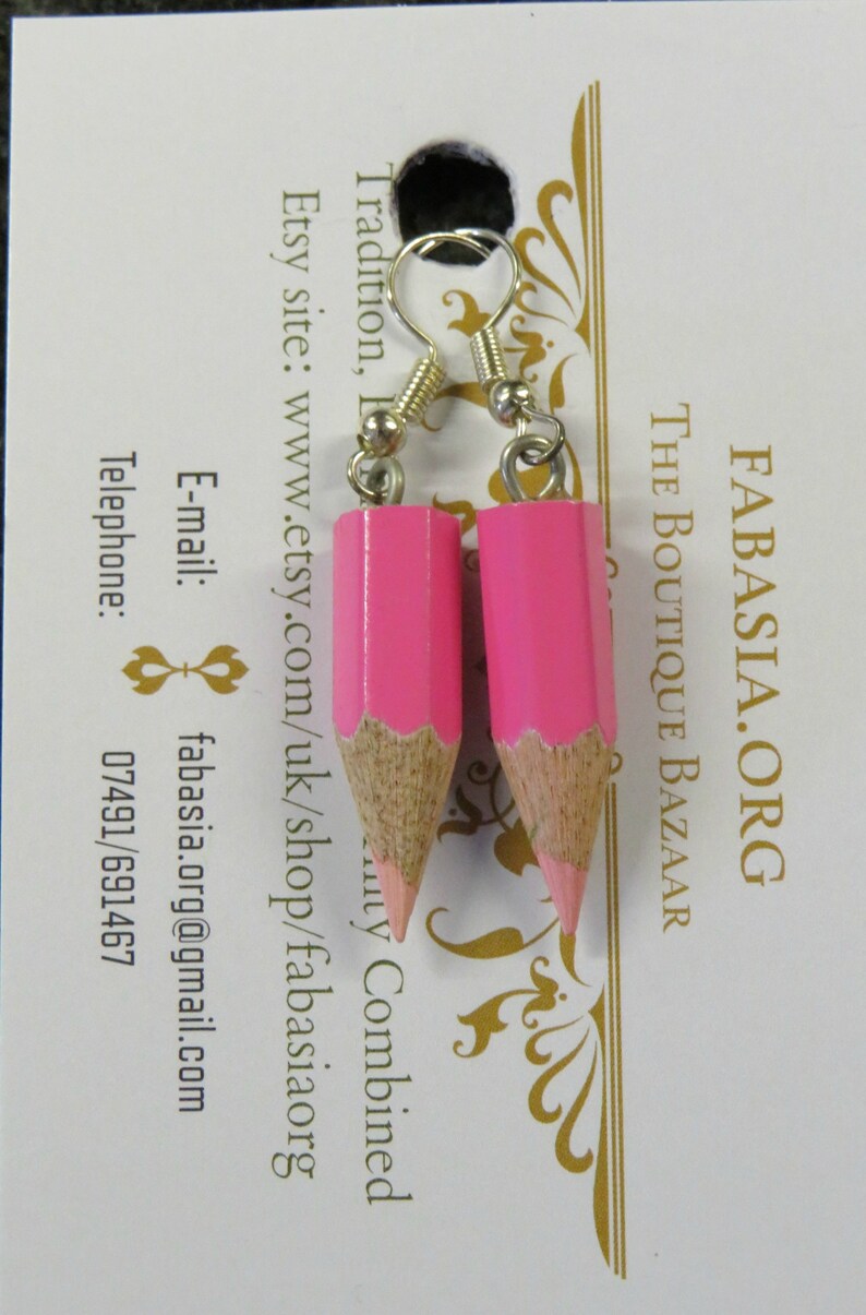 May include: A pair of pink pencil earrings with silver hooks. The pencils are made of wood and have a pink paint finish. The earrings are a fun and unique way to add a touch of personality to any outfit.