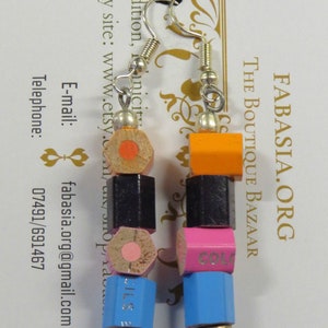May include: A pair of earrings made from colorful pencil ends. The earrings are made of wood and metal. The pencil ends are in the colors orange, black, pink, and blue. The earrings are hanging from silver hooks.
