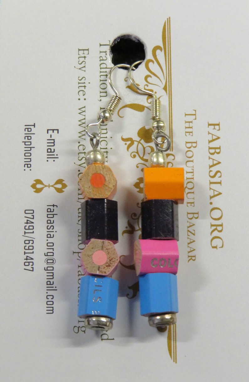 May include: A pair of earrings made from colorful pencil ends. The earrings are made of wood and metal. The pencil ends are in the colors orange, black, pink, and blue. The earrings are hanging from silver hooks.