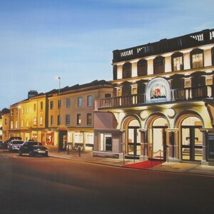 May include: A painting of a city street at night with a theater on the right side of the image. The theater has a red carpet leading up to the entrance. The building is lit up with yellow lights. There are cars parked on the street in front of the theater.