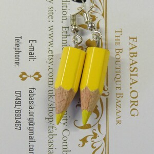May include: A pair of yellow pencil earrings with silver hooks. The earrings are on a white card with the text "FABASIA.ORG THE BOUTIQUE BAZAAR Tradition, Ethnic Etsy site: www.etsy.com/uk/shop/fabasiaorg E-mail: fabasia.org@gmail.com Telephone: 07491/691467"