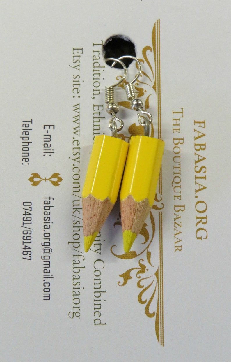 May include: A pair of yellow pencil earrings with silver hooks. The earrings are on a white card with the text "FABASIA.ORG THE BOUTIQUE BAZAAR Tradition, Ethnic Etsy site: www.etsy.com/uk/shop/fabasiaorg E-mail: fabasia.org@gmail.com Telephone: 07491/691467"